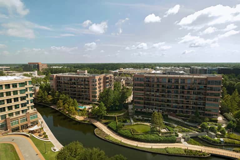 Aerial view of modern residential complex with landscaping along waterway and greenery