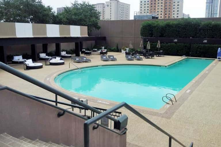 Urban hotel rooftop pool with turquoise water, lounge chairs, and city skyline backdrop