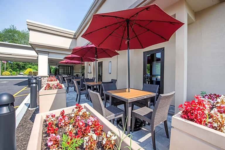 Outdoor patio with red umbrellas, dining tables, and flowering planters