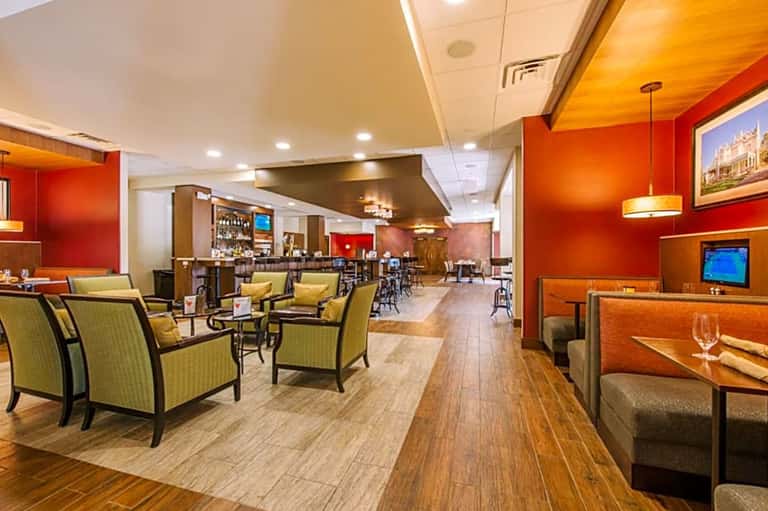 Upscale hotel bar and lounge with red accent walls, green chairs, bar counter, and warm lighting