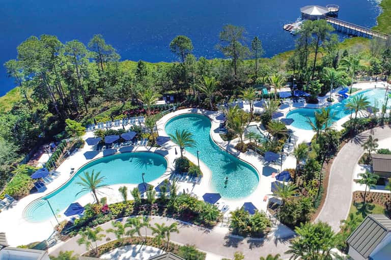 Aerial view of sprawling resort pools with winding lazy river, palm trees, and forested surroundings