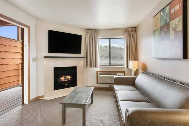 Hotel room with fireplace, flat-screen TV, beige sofa, and glass door to private balcony