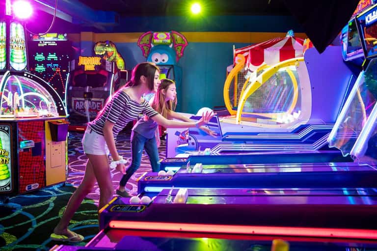 Family playing neon glow-in-the-dark mini golf with colorful illuminated obstacles and arcade games