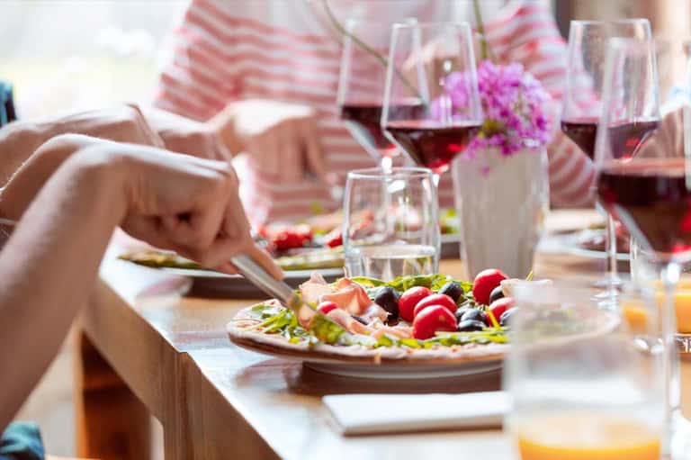 Elegant outdoor dining table with wine glasses, fresh appetizers, flowers, and striped umbrella