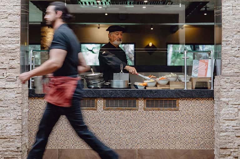 Restaurant kitchen window with chef preparing food while pedestrian walks by on street