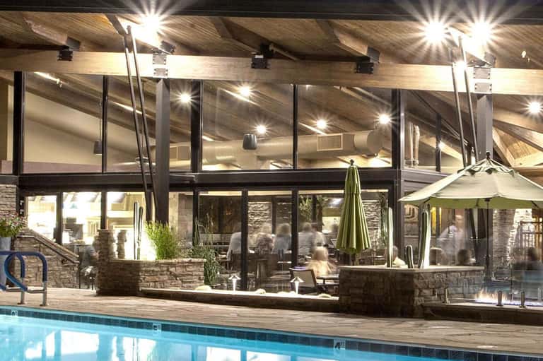 Illuminated poolside pavilion at night with stone accents, lounge chairs, and modern architectural design