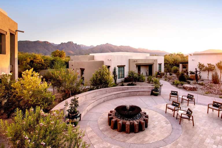 Desert resort courtyard with circular fire pit, lounge chairs, and mountain sunset views