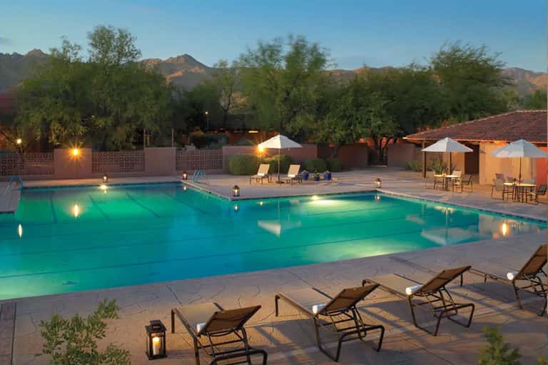 Illuminated resort pool at dusk with lounge chairs and mountain backdrop