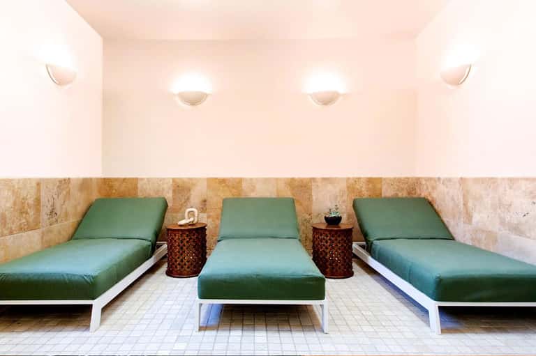 Spa relaxation area with three green lounge chairs and travertine tile walls