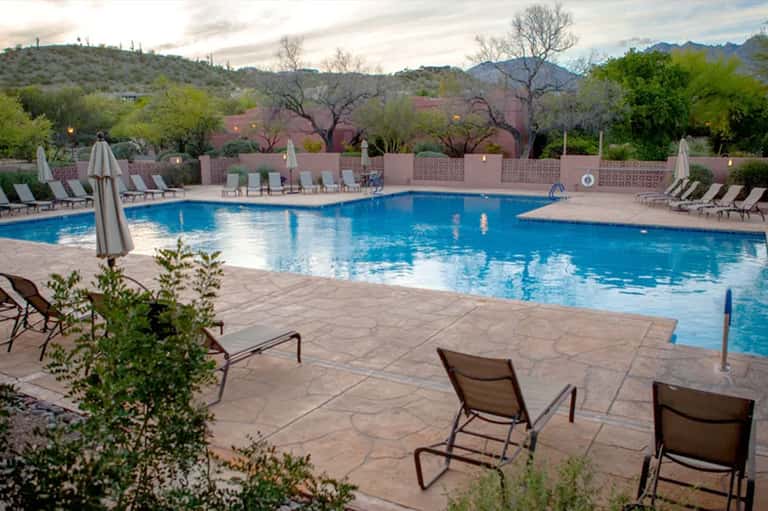 Expansive resort pool with desert mountain backdrop, lounge chairs, umbrellas, and surrounding landscaping