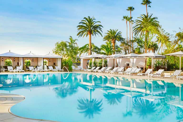 Turquoise resort pool with palm trees, white cabanas, and lounge chairs under blue sky