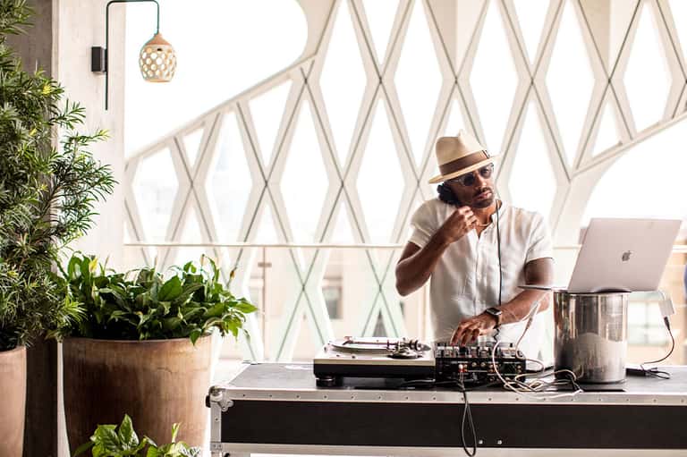 DJ performing at an outdoor event with geometric white lattice backdrop and potted plants