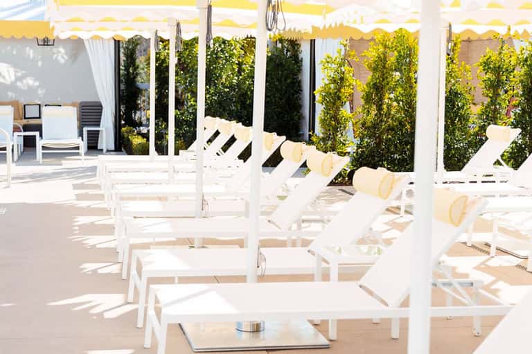 White lounge chairs with yellow umbrellas under a covered patio with ivy-covered walls