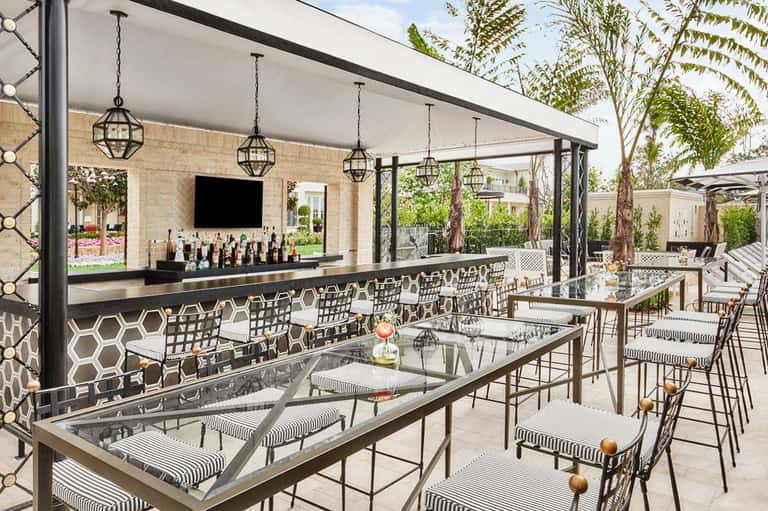 Upscale outdoor bar and lounge with black patterned bar seating, hanging lights, and lush greenery