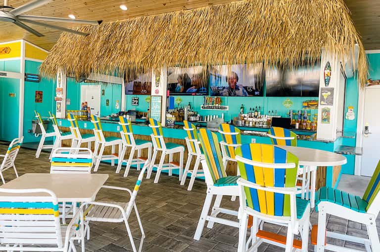 Tropical tiki bar with turquoise walls, striped chairs, thatched roof, and casual island atmosphere