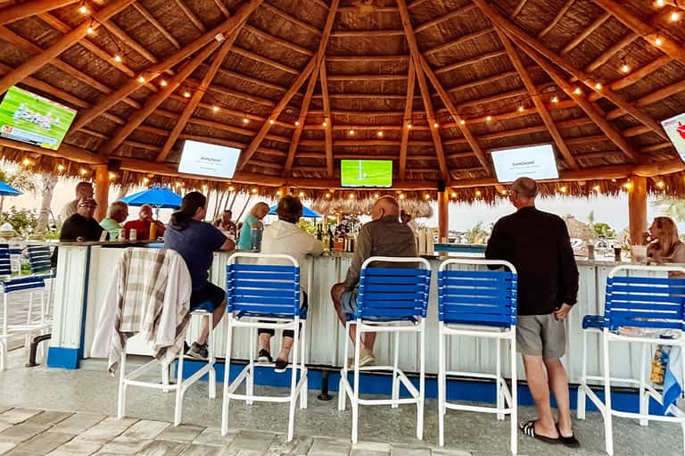 Tiki bar with thatched roof, wooden structure, blue lounge chairs, and ocean backdrop