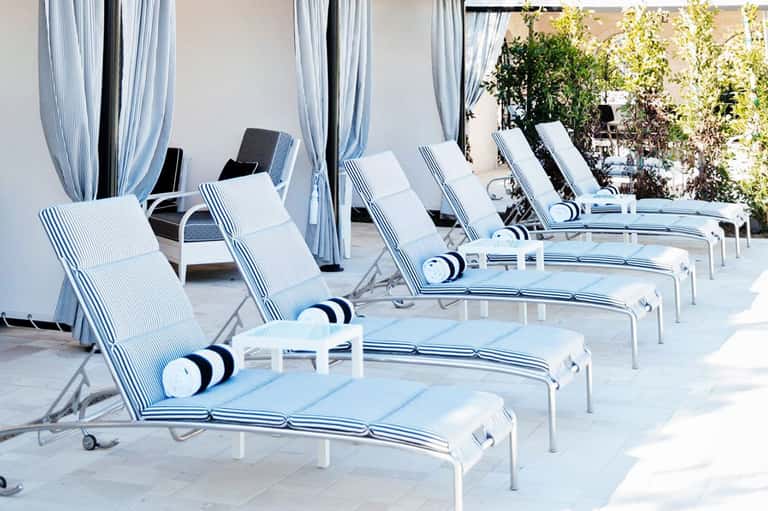Row of striped lounge chairs with blue and white cushions on a sunny terrace with curtained cabanas