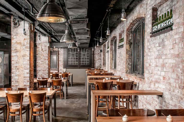 Industrial-style dining space with brick walls, wooden tables, pendant lighting, and metal structural beams