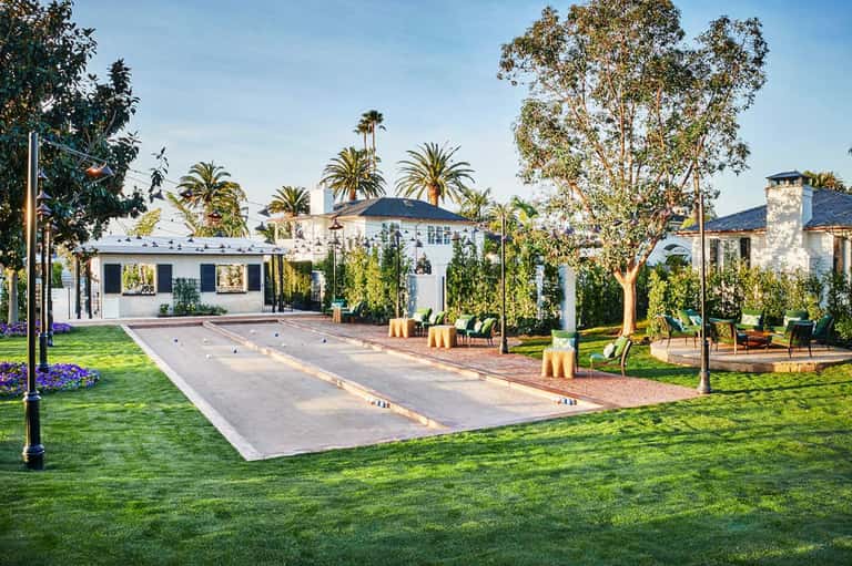 Luxury estate with bocce ball court, manicured lawn, palm trees, and white Mediterranean-style mansion