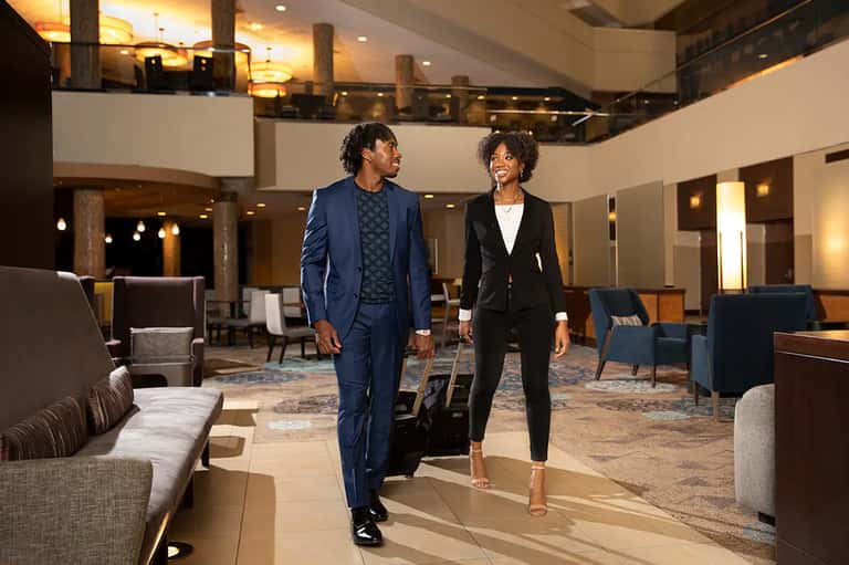 Man and woman in business attire walking through elegant hotel lobby with high ceilings