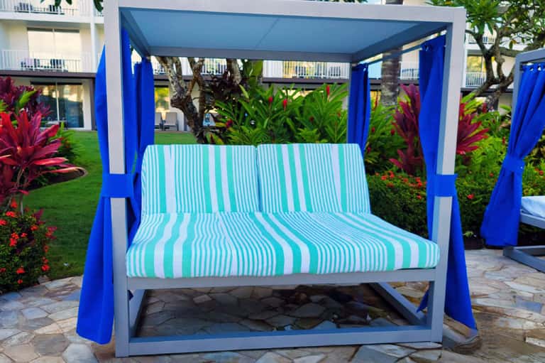 Modern blue and white cabana bed with striped cushions set on stone patio overlooking manicured lawn