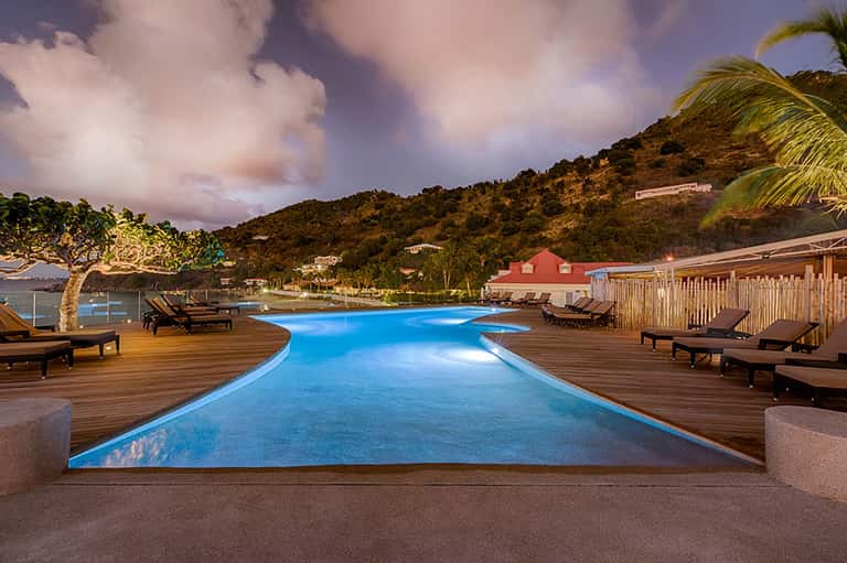 Illuminated resort pool at dusk with lounge chairs and tropical hillside setting