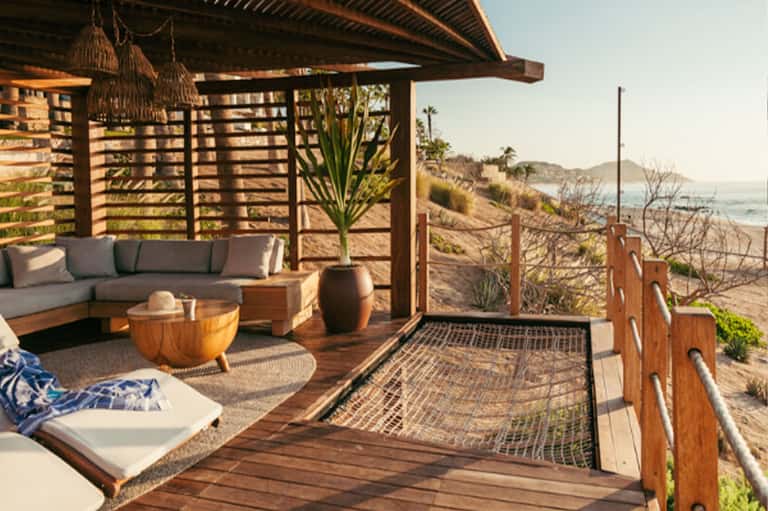 Elevated wooden deck with gray cushioned seating, pergola shade, and coastal ocean views