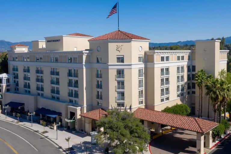 Large beige hotel building with terra cotta roof, American flag, and mountains visible in background