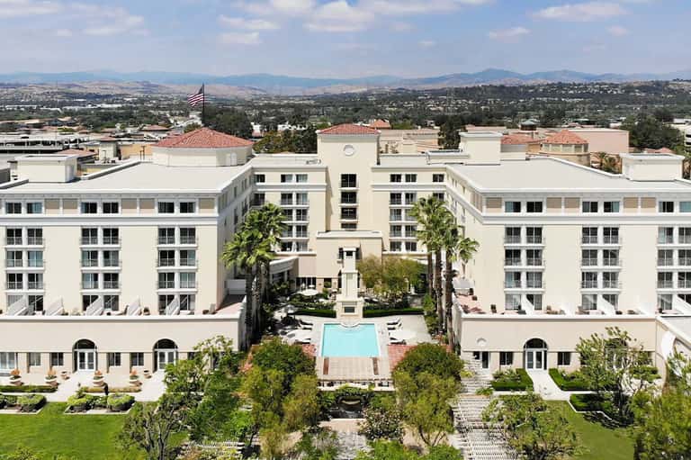 Aerial view of white resort complex with central courtyard pool surrounded by palm trees