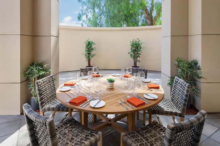Circular wooden dining table set for four in courtyard with plants and curved walls