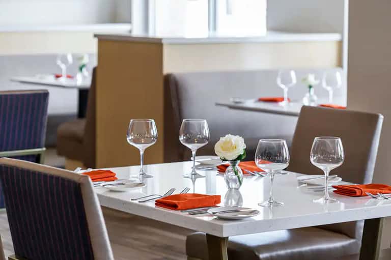 Elegant dining table set with wine glasses, white flower centerpiece, and orange napkins