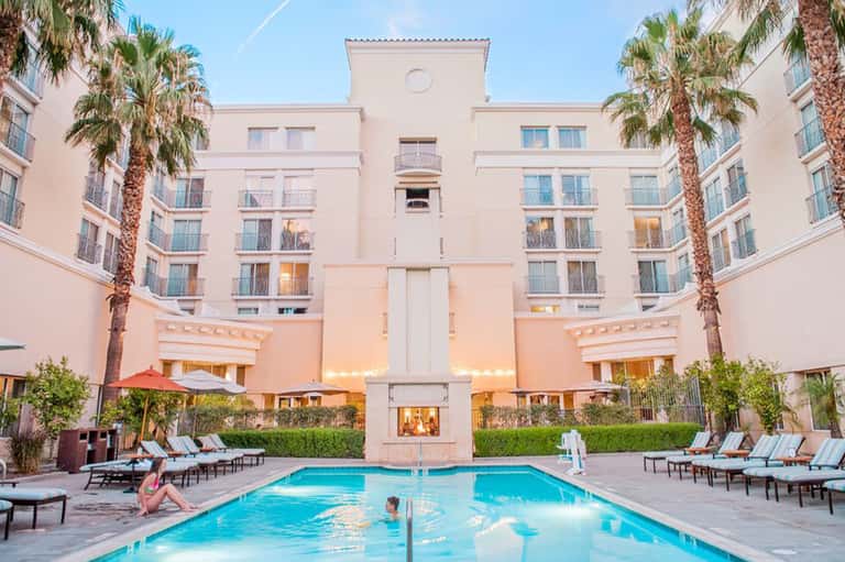 Resort courtyard pool surrounded by pink building with palm trees and lounge chairs
