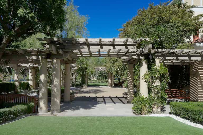 Garden pergola pathway with white lattice structure, green landscaping, and sunny blue sky