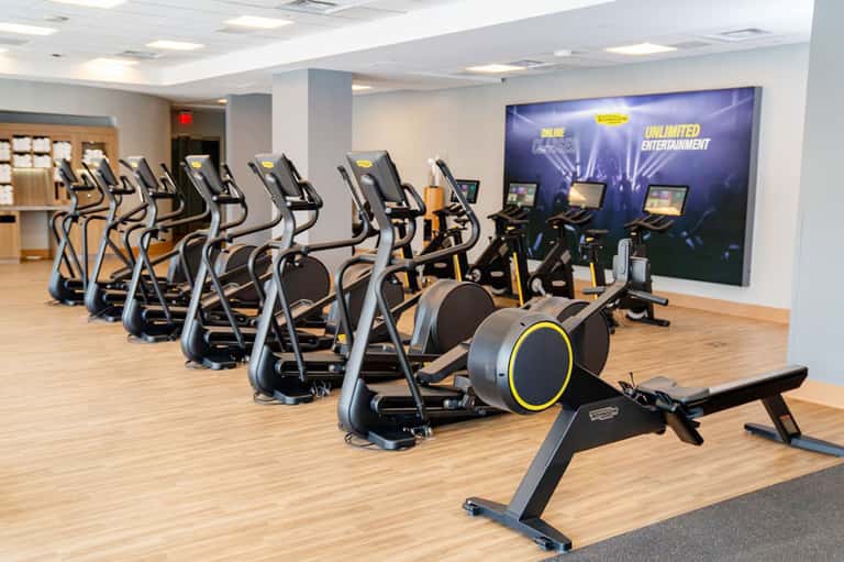 State-of-the-art fitness facility with rows of elliptical machines and large entertainment screen