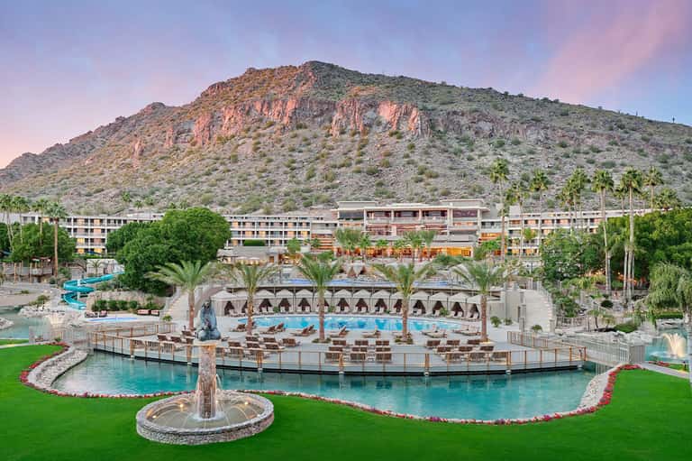 Sprawling desert resort with multiple pools, palm trees, mountain backdrop, and modern architecture