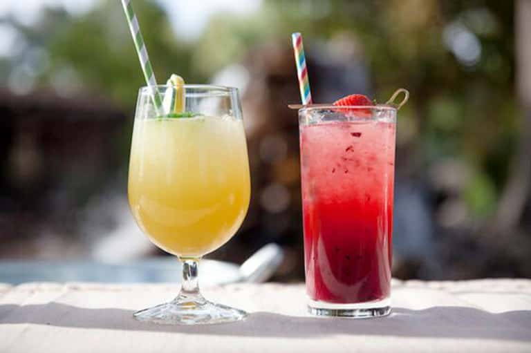 Two refreshing tropical beverages with colorful straws and fruit garnishes on sandy beach