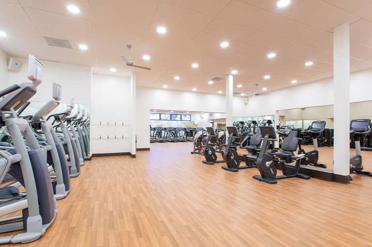 Spacious gym with cardio machines, stationary bikes, mirrors, and wooden flooring