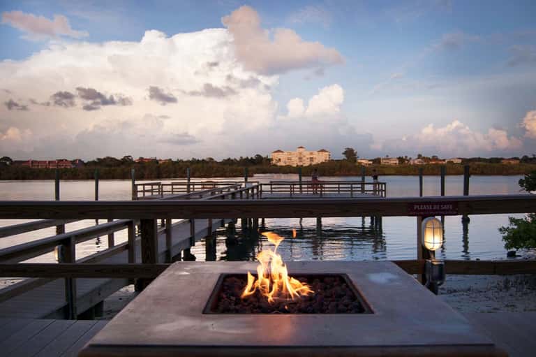 Waterfront fire pit with dock overlooking calm bay and resort building at dusk