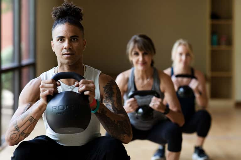 Fitness instructor holding kettlebell during group workout class with participants in background