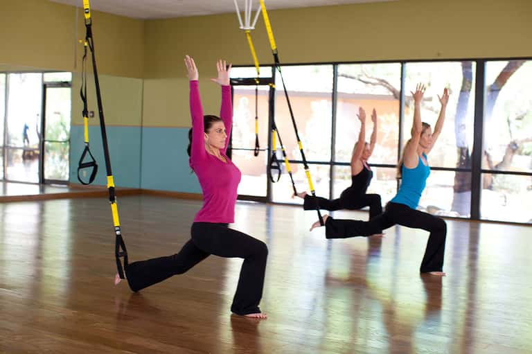 Fitness class doing suspension training exercises in bright gym with ocean view