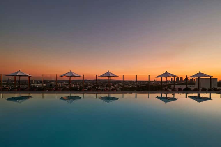 Infinity pool at dusk with umbrellas and city skyline reflection at sunset