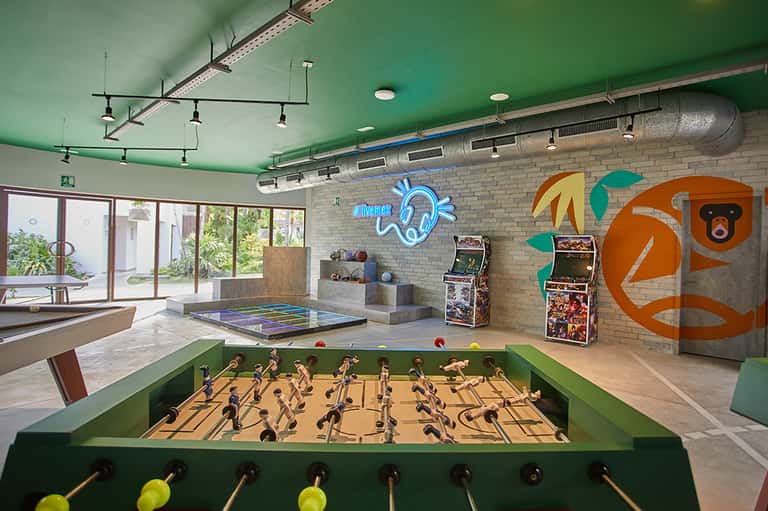 Recreation room with green foosball table, arcade games, ping pong table, and neon signage
