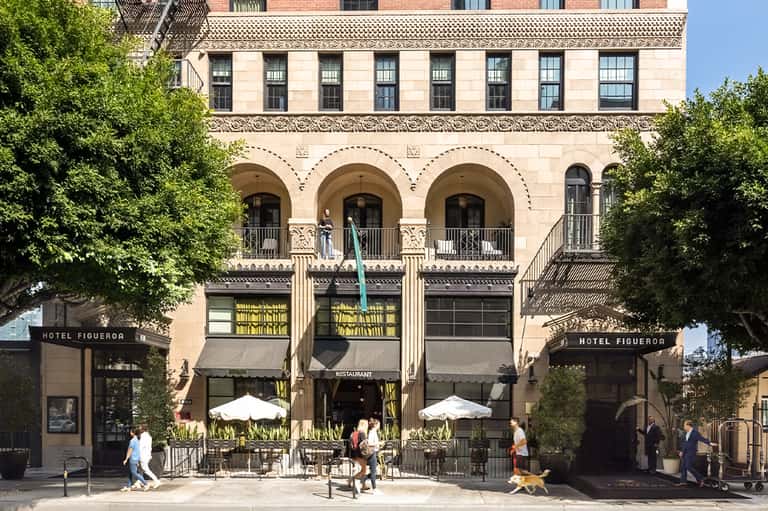 Historic hotel building facade with arches, columns, green awnings, and outdoor dining area
