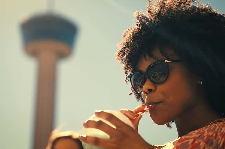 Woman with sunglasses eating while water tower blurs in background, daytime travel shot