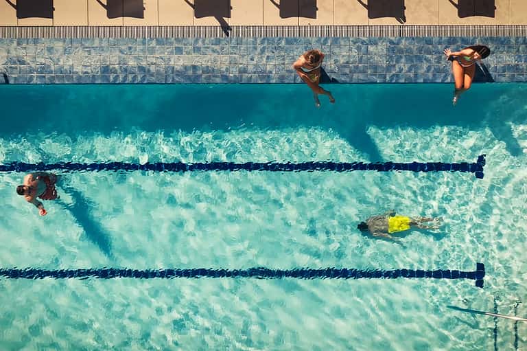 Overhead view of swimmers in lap pool with lane dividers and clearly visible water