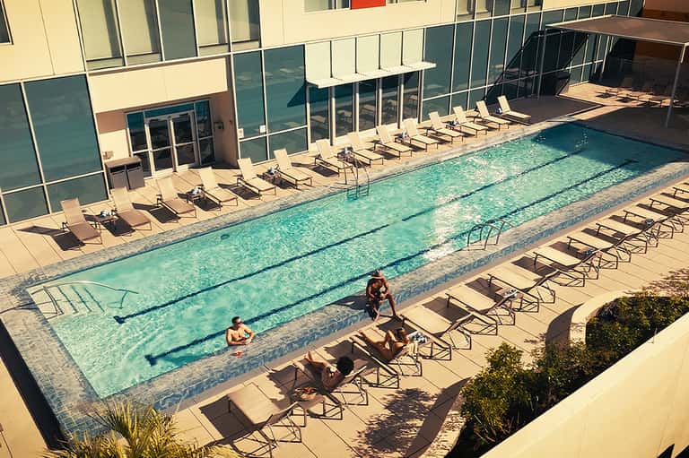 Lap pool with swimmers and lounge chairs along a modern hotel building