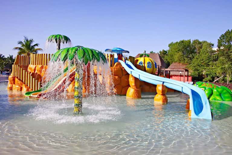 Colorful water park with palm tree water features and blue slides in tropical setting
