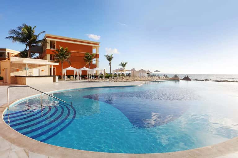 Beachfront infinity pool overlooking ocean with orange building and white cabanas