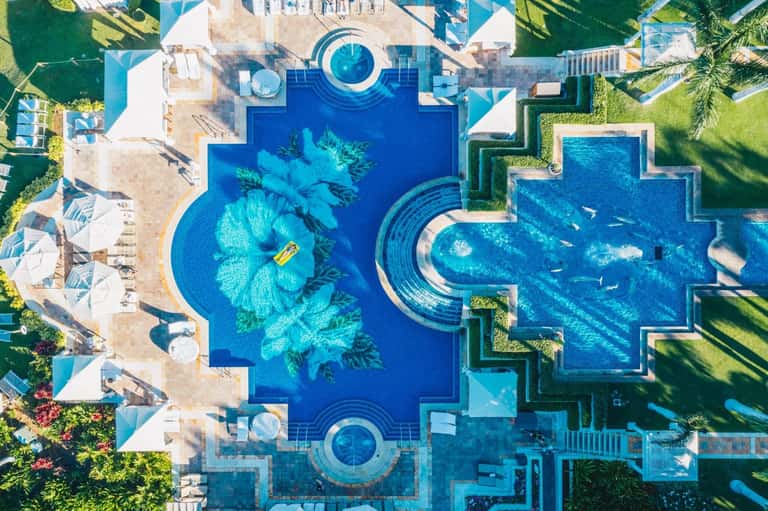 Aerial view of elaborate resort pools with geometric shapes and tropical landscaping