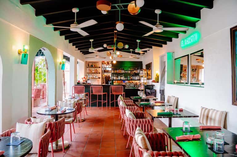 Modern restaurant interior with colorful ceiling details, bar, dining tables, and neon signage
